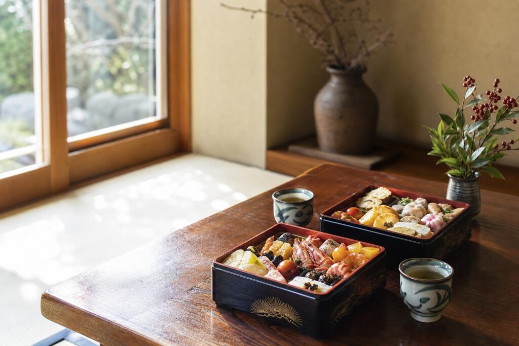 和室の机に置かれた正月のおせち料理と湯のみ